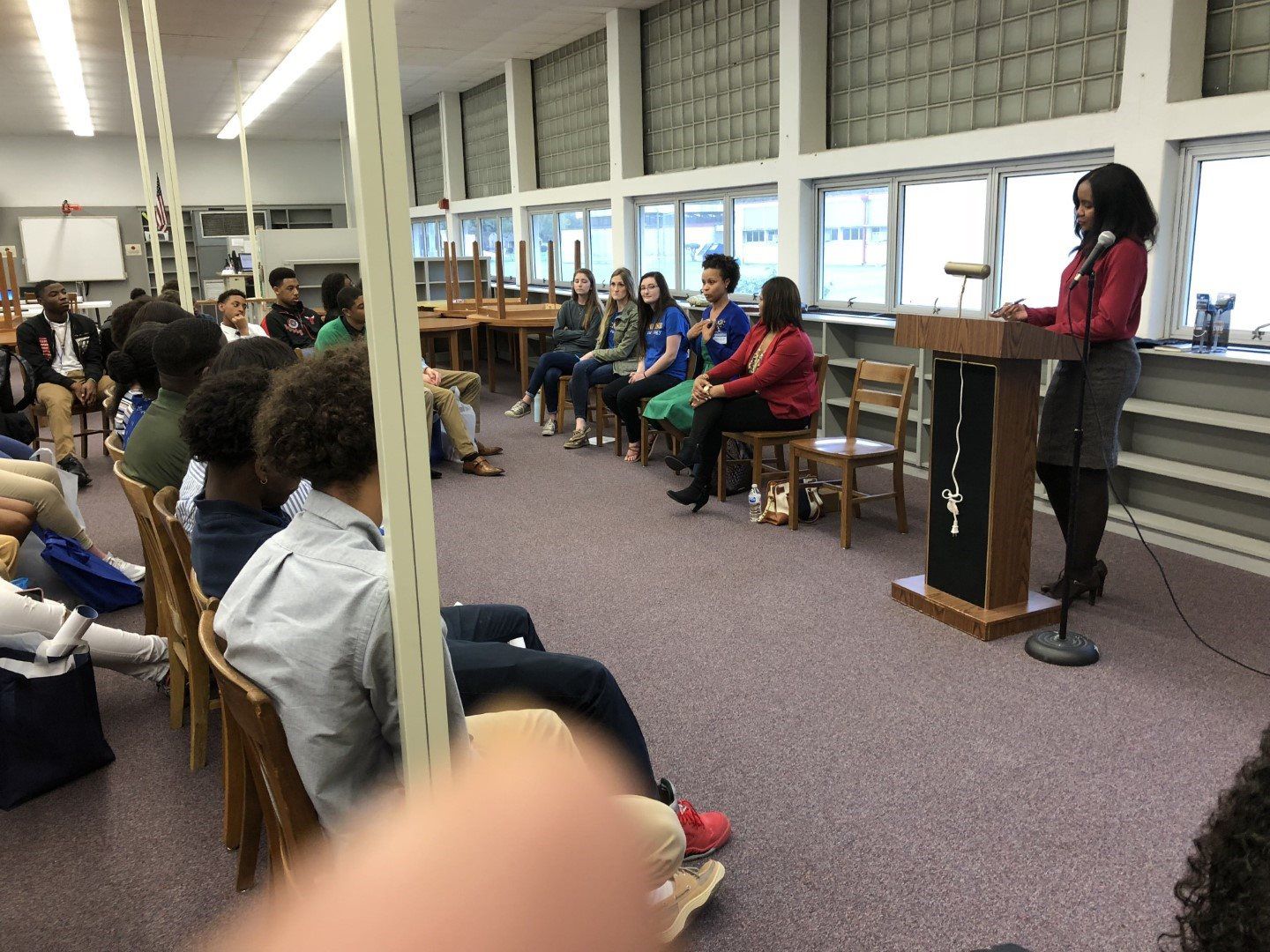 A woman is standing at a podium giving a presentation to a group of people sitting in chairs.