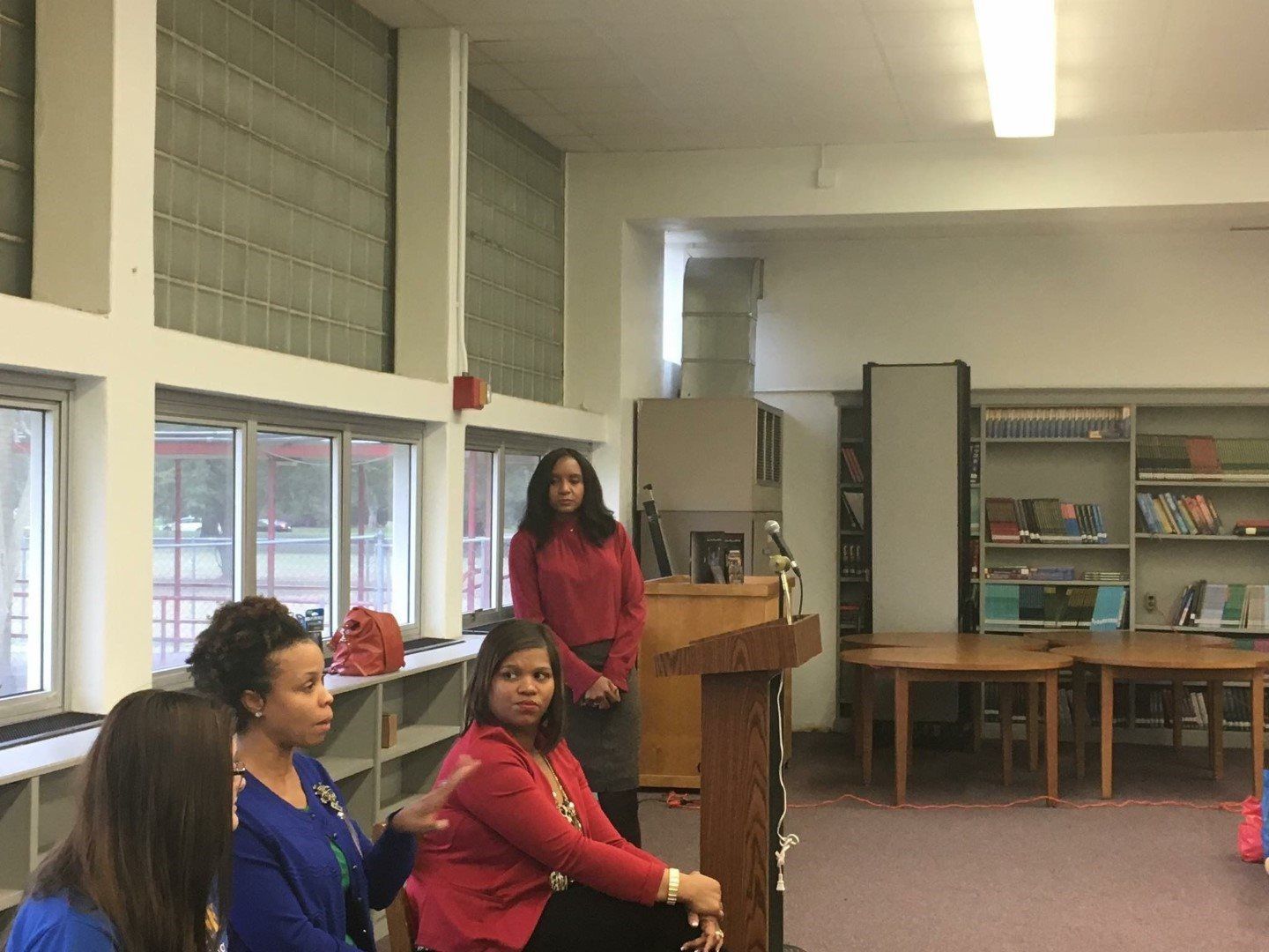A group of women are sitting around a podium in a library.