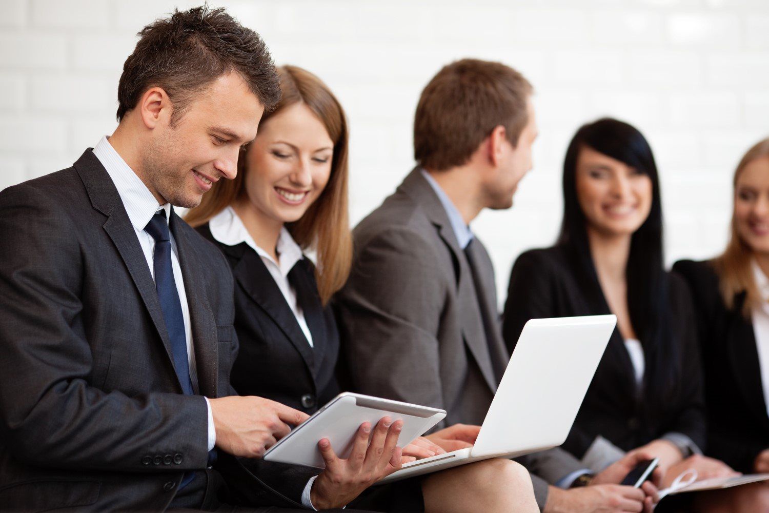 A group of business people are sitting in a row with laptops and tablets