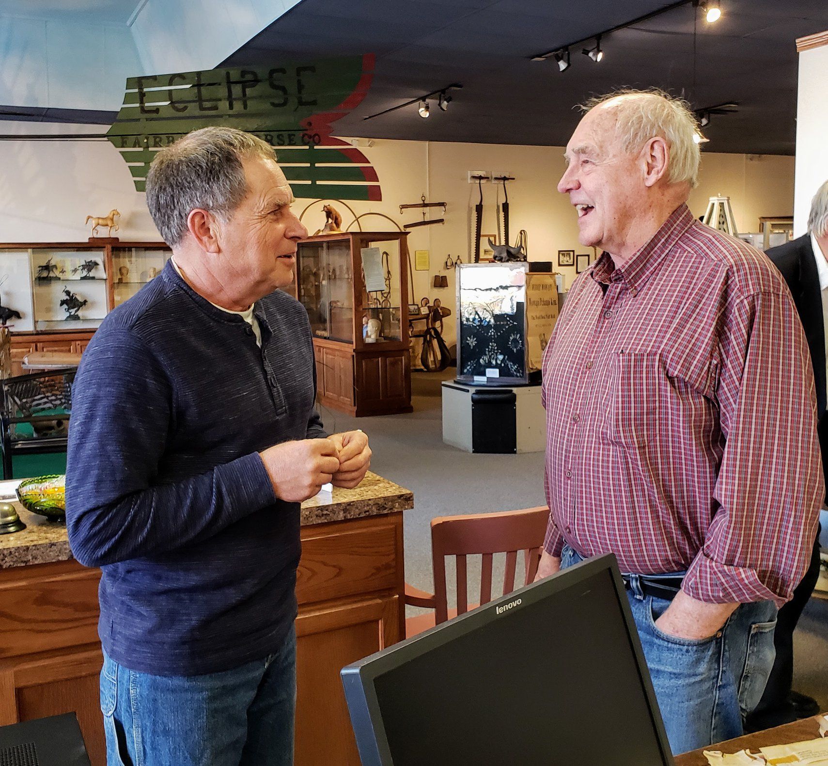 Two men conversing in a museum. One wears a blue shirt, the other a red patterned shirt.