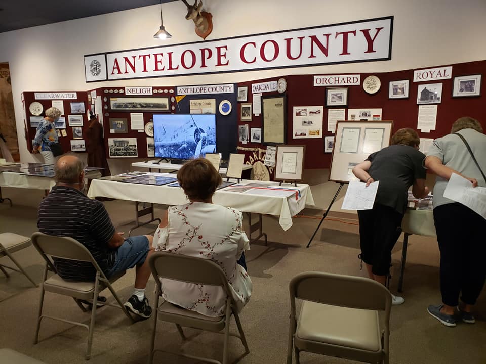People view exhibits at Antelope County museum. Displays include photos, a screen, and information.