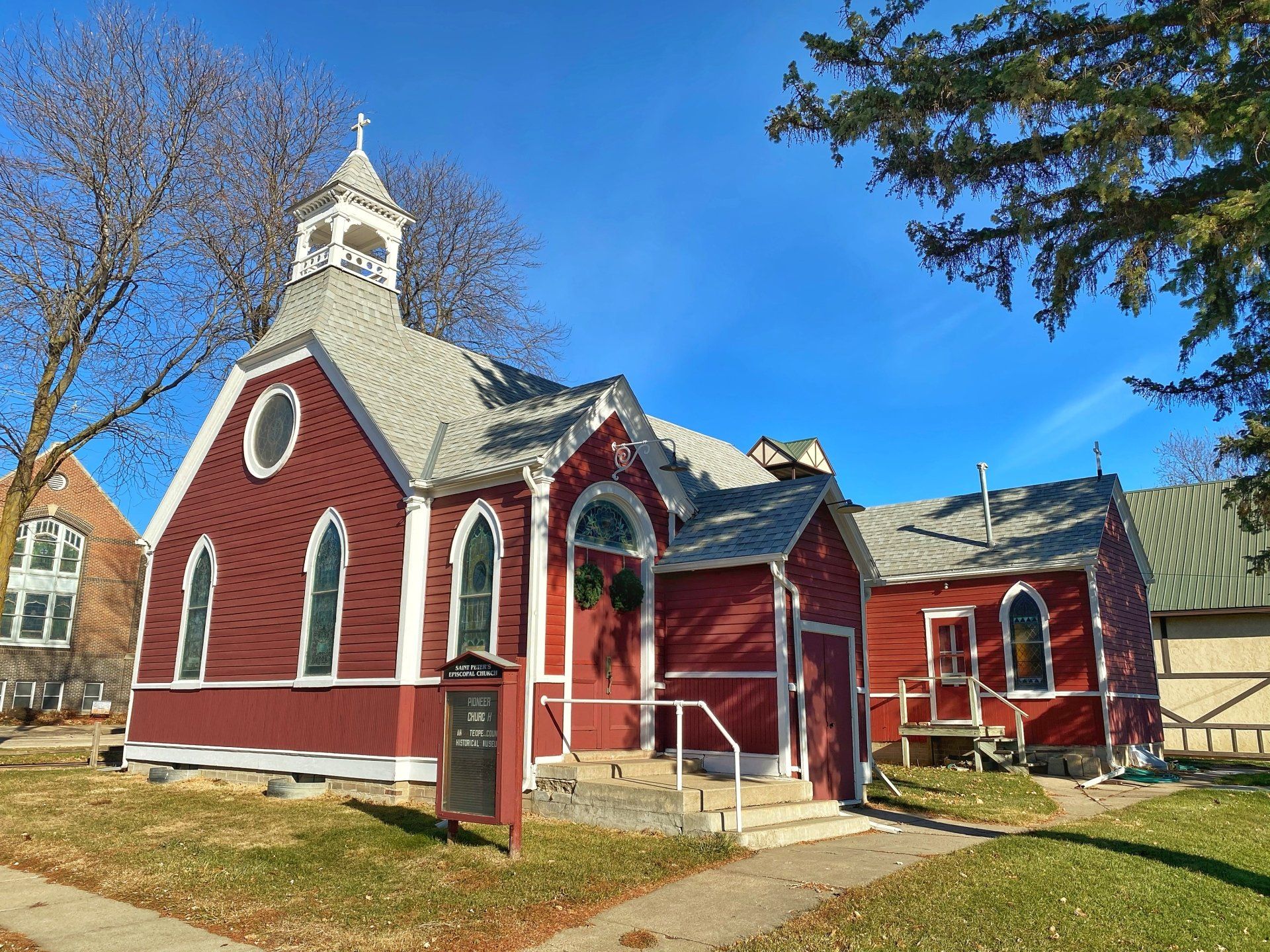 Red wooden church with white trim against a blue sky, autumn leaves on the ground.