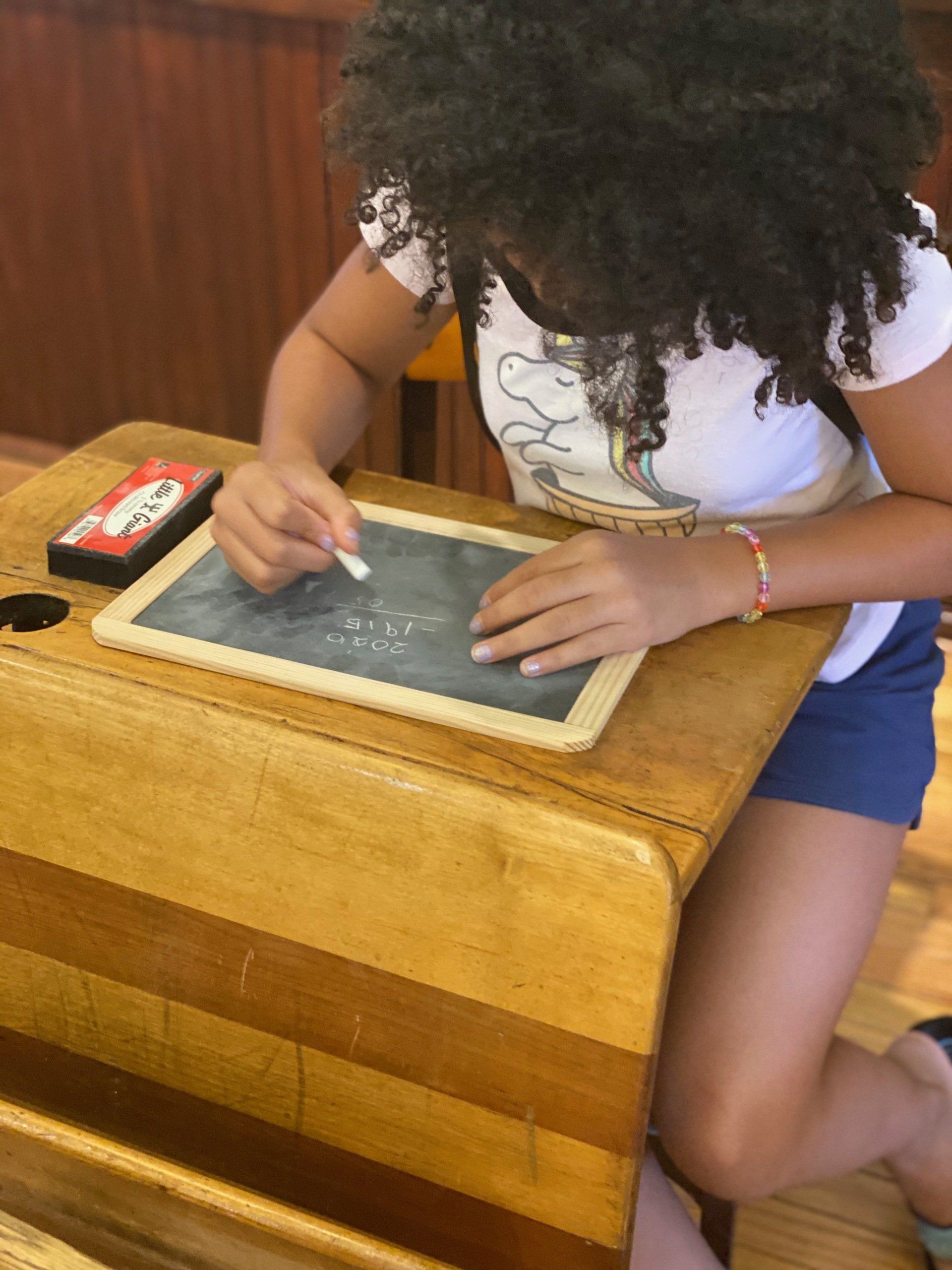 Girl writing on a chalkboard at a vintage school desk.