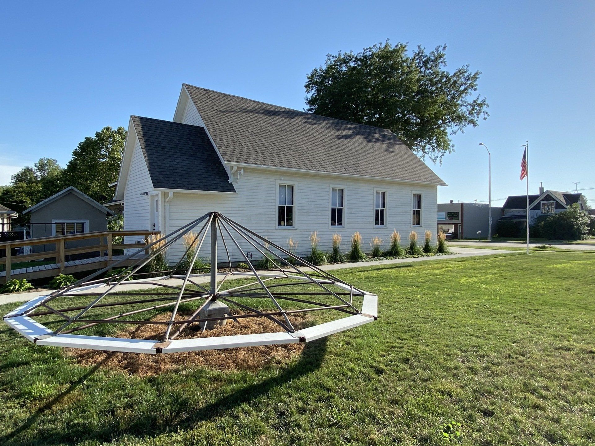White building with a gray roof and a merry-go-round in front; sunny day.