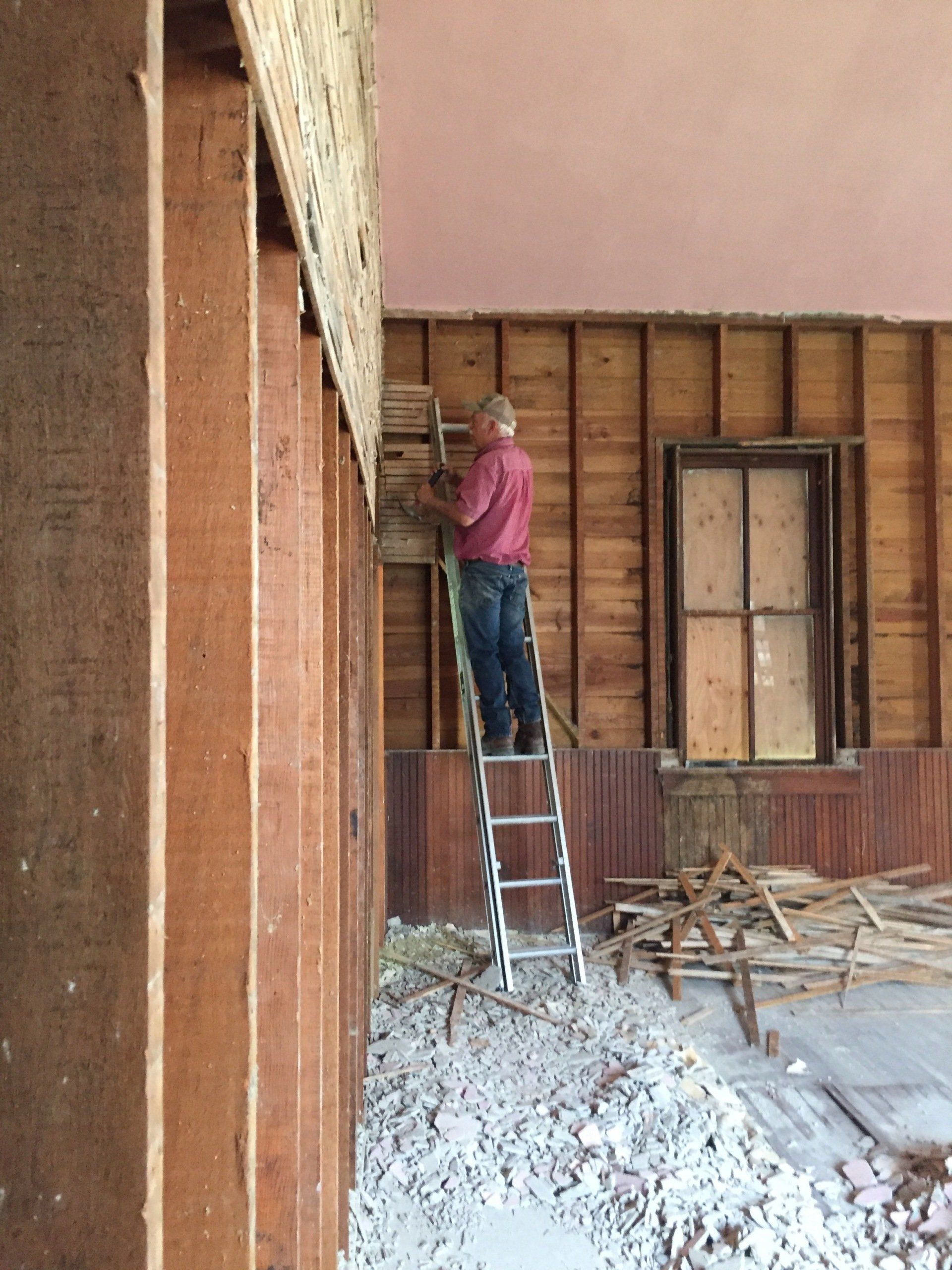 Man on ladder removing wall during renovation, interior setting.