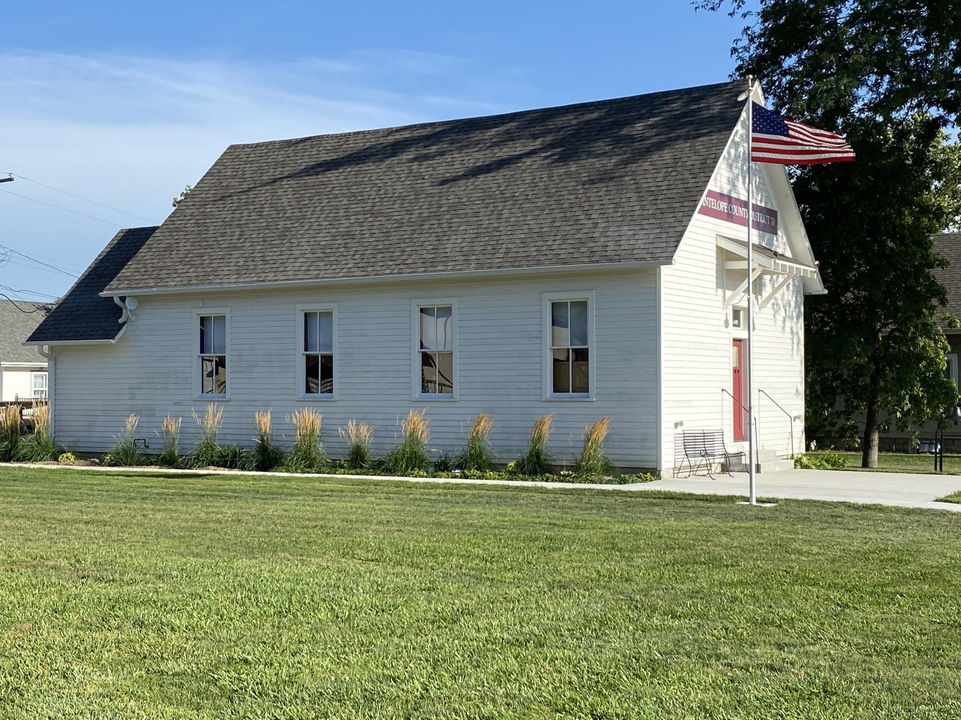 White, one-room schoolhouse with American flag in front yard on a sunny day.