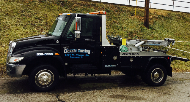 Black tow truck parked outdoors with a crane arm and “Classic Towing” on the door.