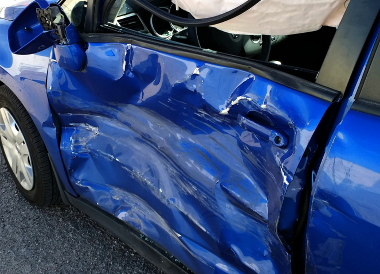 Severely dented blue car door after collision, with crumpled metal and open window.