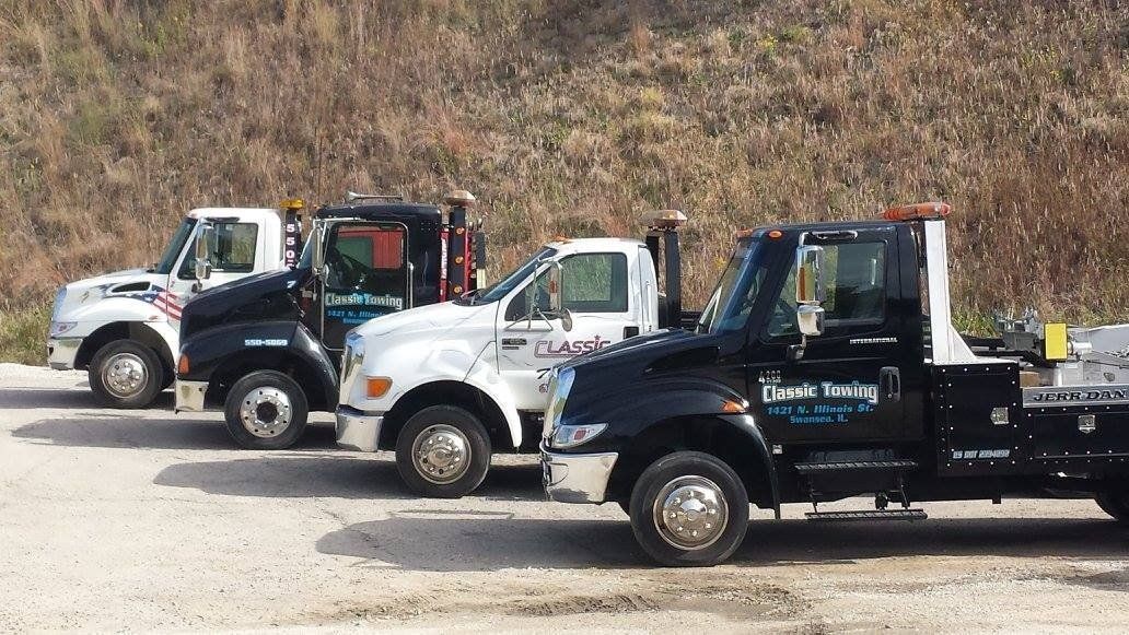 Three tow trucks parked in a row on a gravel lot with dry brush in the background
