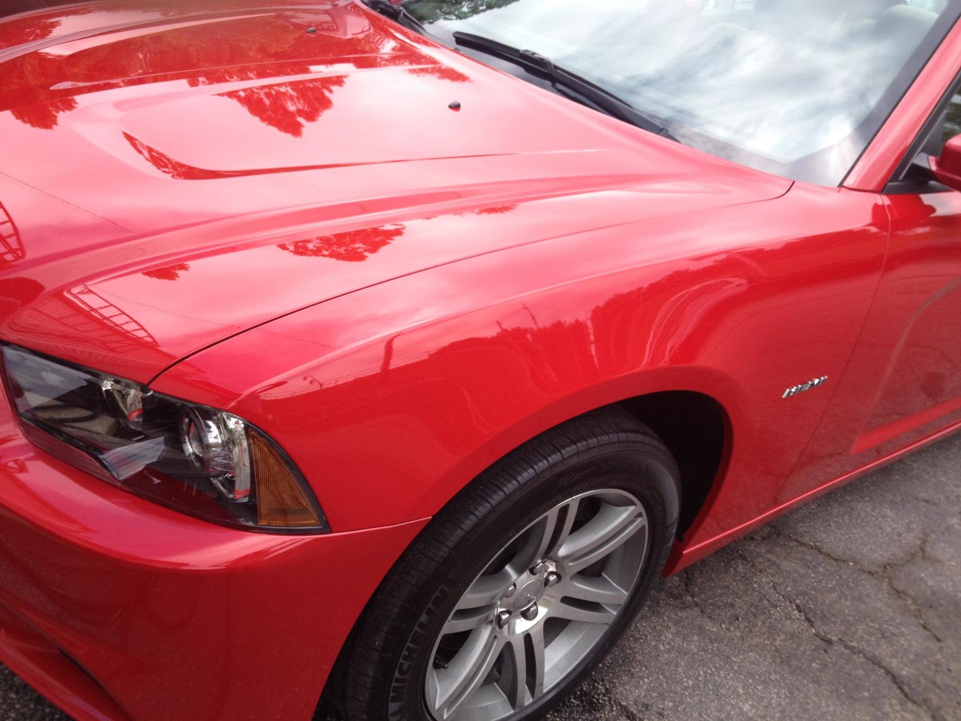 Red sports car parked on pavement, close-up of hood, headlight, and front wheel.