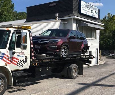 Tow truck hauling a maroon SUV in front of a small white building.