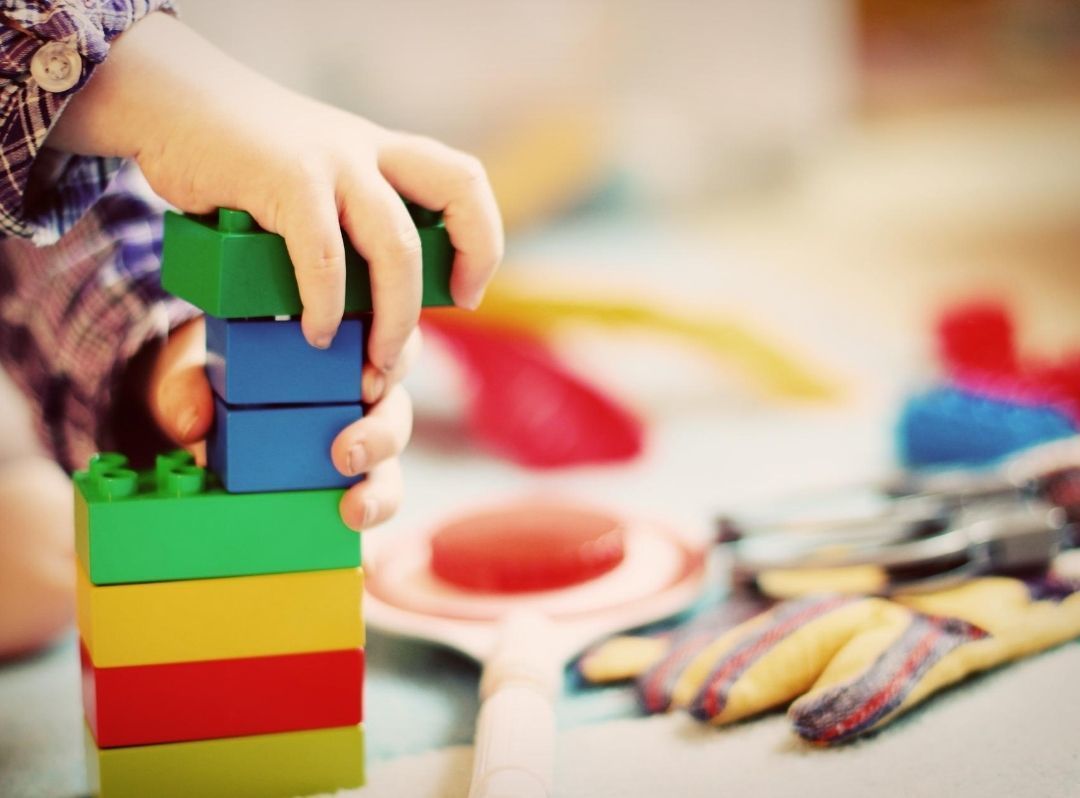 Hand stacking colorful wooden blocks on a table with toy tools in the background