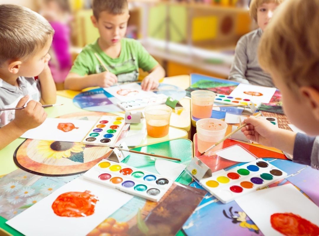 Children painting at a table with colorful art supplies and paint palettes