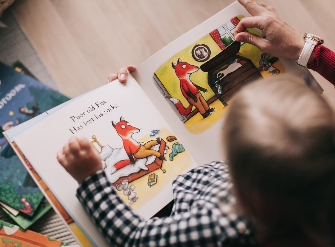 Child reading a colorful picture book with an adult on a couch