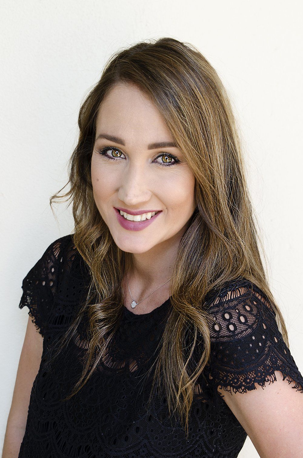 Smiling person in a black lace top against a plain white background