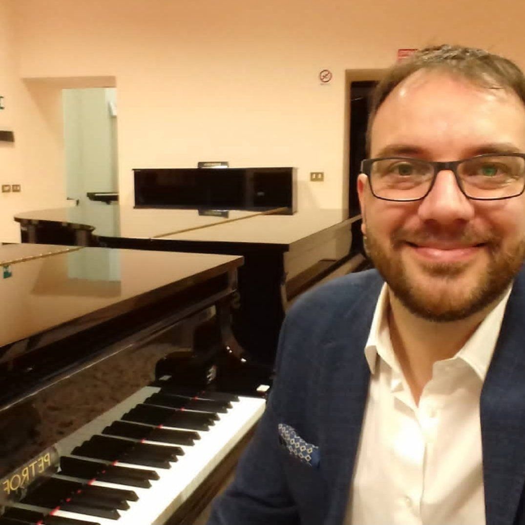Un uomo con gli occhiali è seduto davanti a un pianoforte su cui è scritto 