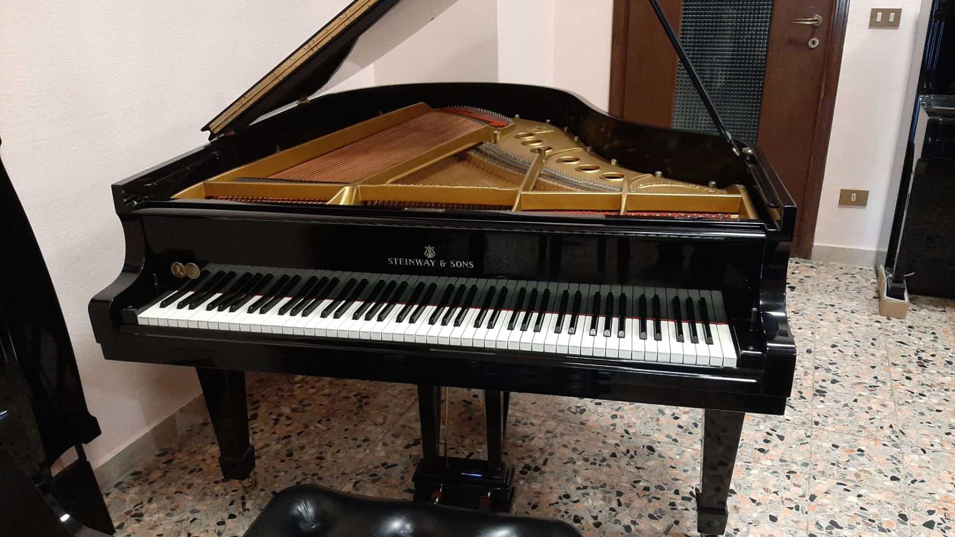 Un pianoforte a coda nero è appoggiato su un pavimento piastrellato