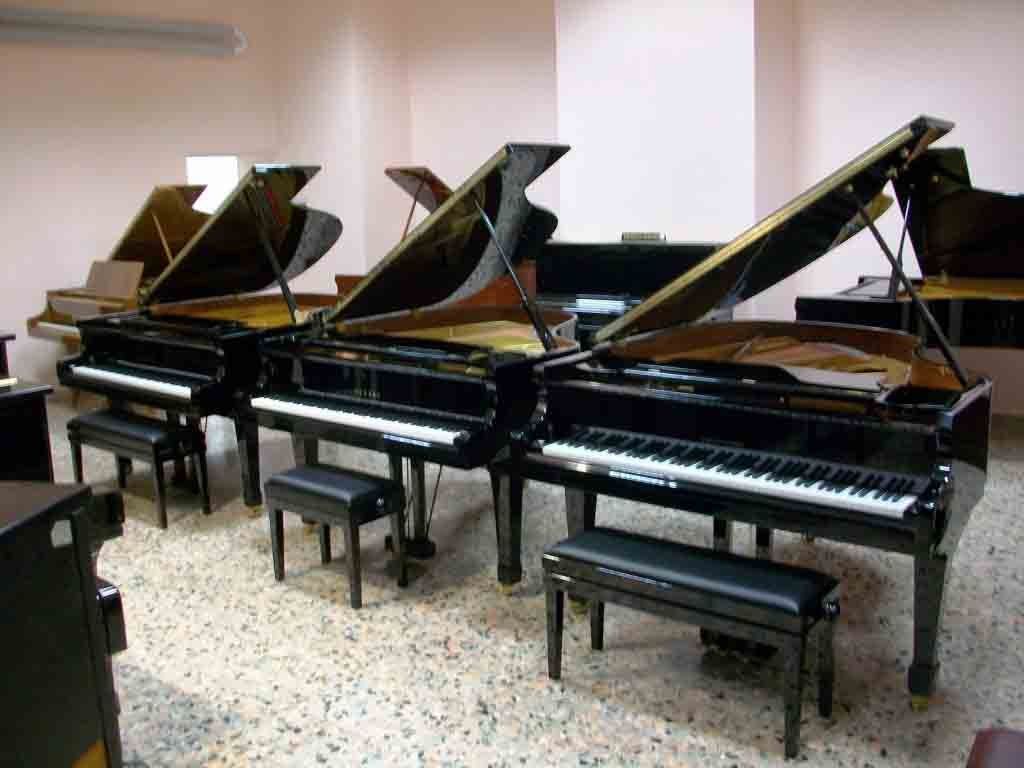 Tre pianoforti sono allineati in una stanza con i coperchi aperti