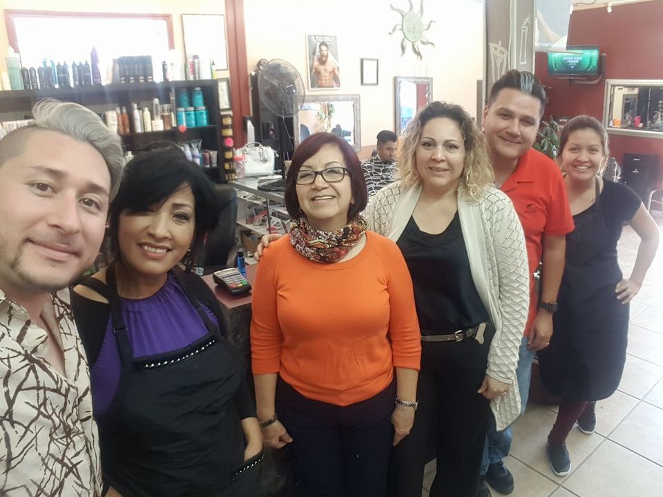 Group of six people smiling in a hair salon. Some are wearing aprons.