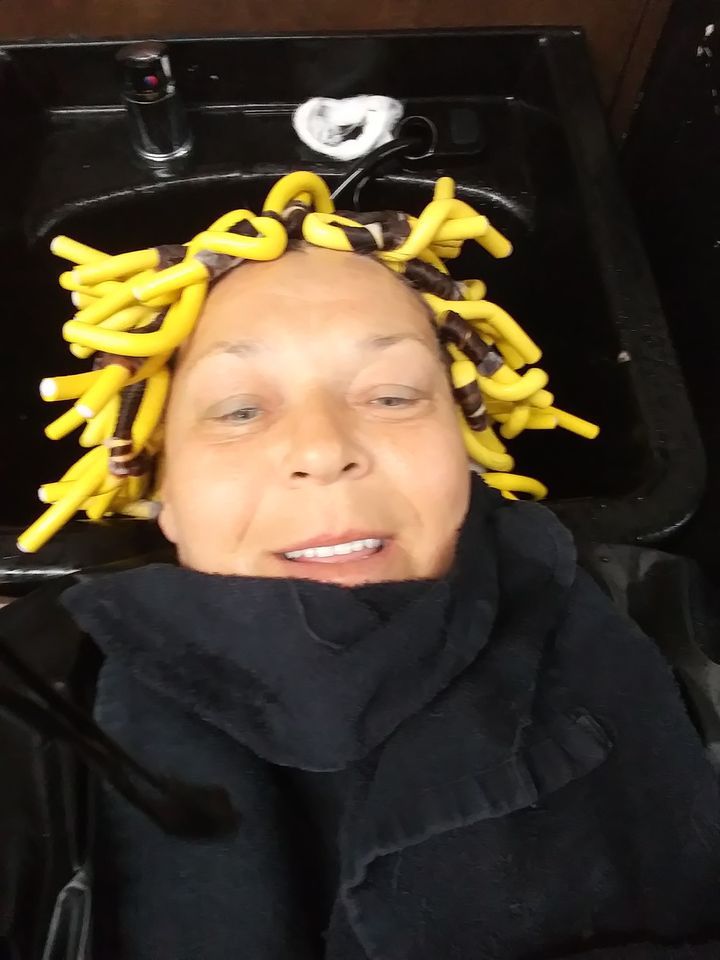 Woman with yellow flexi rods in hair, black towel, in a salon sink.