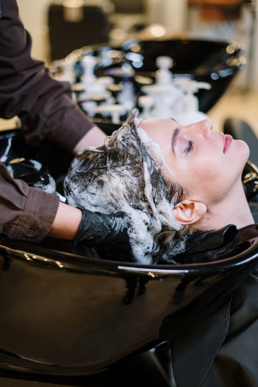 Woman getting her hair washed in a salon sink. Hands with black gloves lather hair with shampoo.