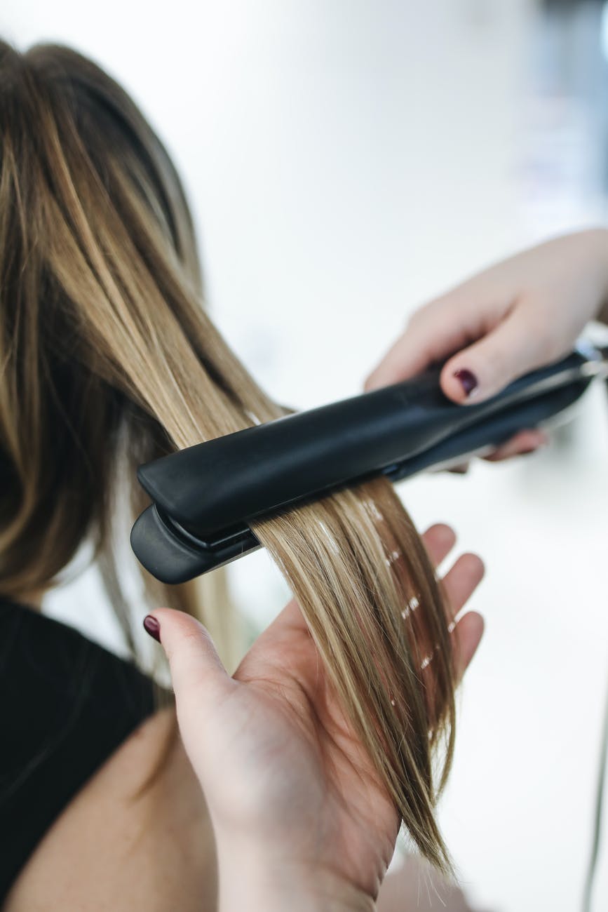 Hair being straightened with a flat iron. Blonde and brown hair with hands in frame.
