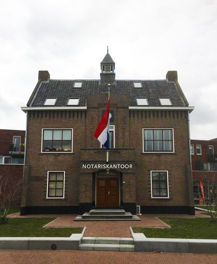 Een bakstenen notariskantoor in Nederland met een Nederlandse vlag boven de ingang.
