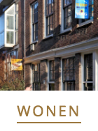 Bakstenen gebouwen met uithangborden in de ramen, waaronder een blauwe makelaarsbanner, met daarboven het woord 