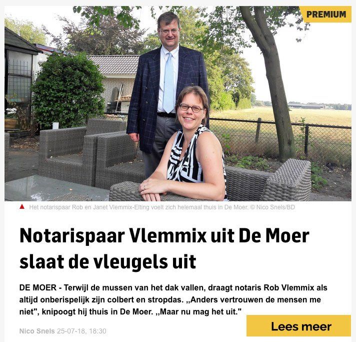 Een man in pak en een vrouw zitten samen op rieten tuinmeubelen buiten in een landelijke omgeving.