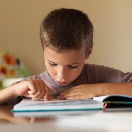 Portrait of focused boy reading a book while sitting at table at home