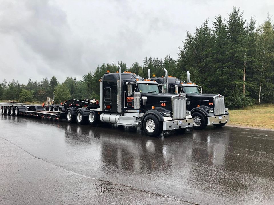 Material Hauling — Backhoe in an Open Trailer in Marquette, MI Material Hauling — Backhoe in an Open Trailer in Marquette, MI