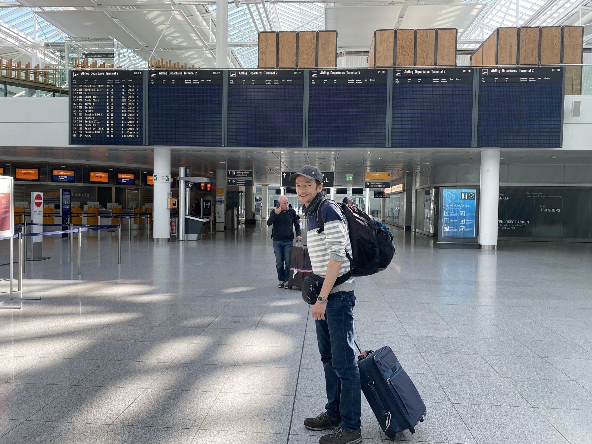 Traveler with backpack and rolling suitcase in a bright airport terminal.