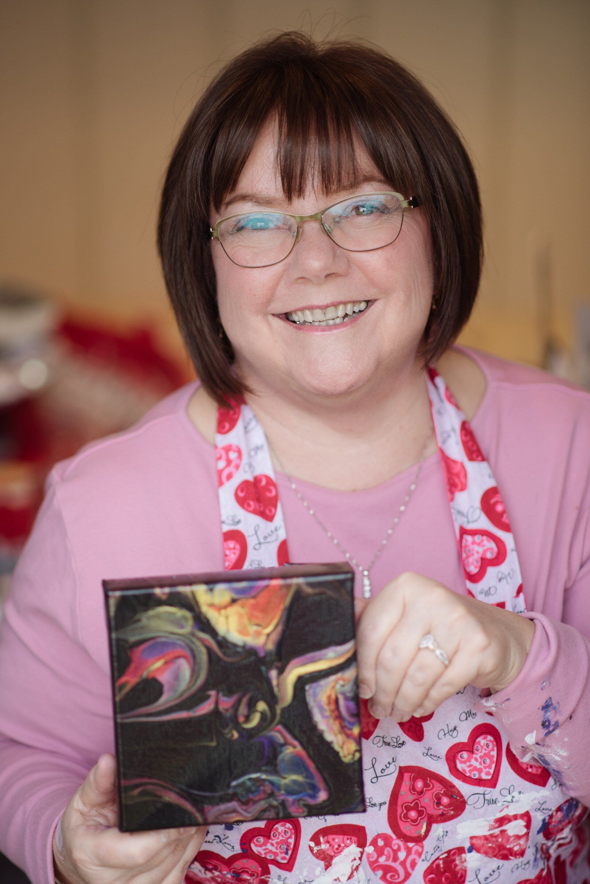 Smiling person in a pink apron holding a small abstract painting
