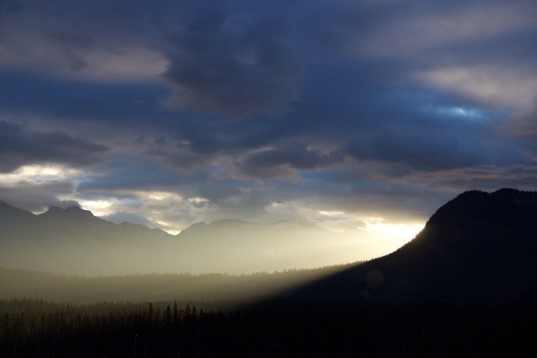 Dramatic cloudy sunset over a mountain valley with dark silhouetted hills and misty light