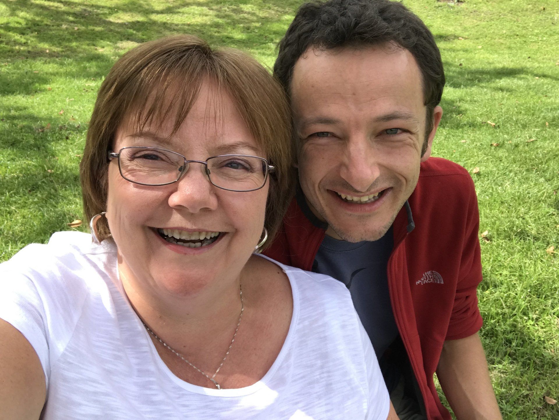 Smiling couple outdoors on green grass, close together and looking at the camera.