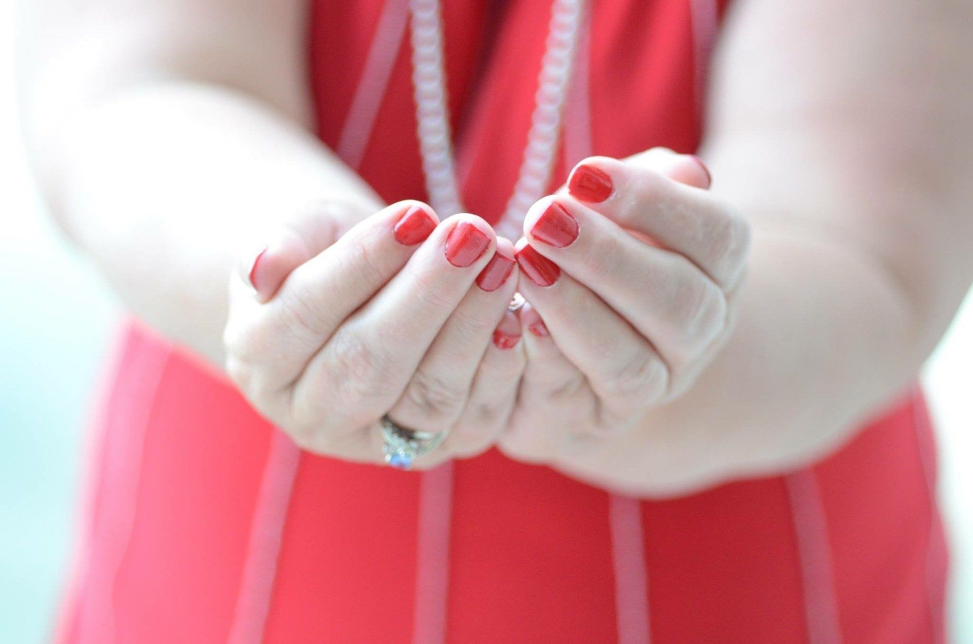 Outstretched hands with red-painted nails holding a small flower, wearing a red dress