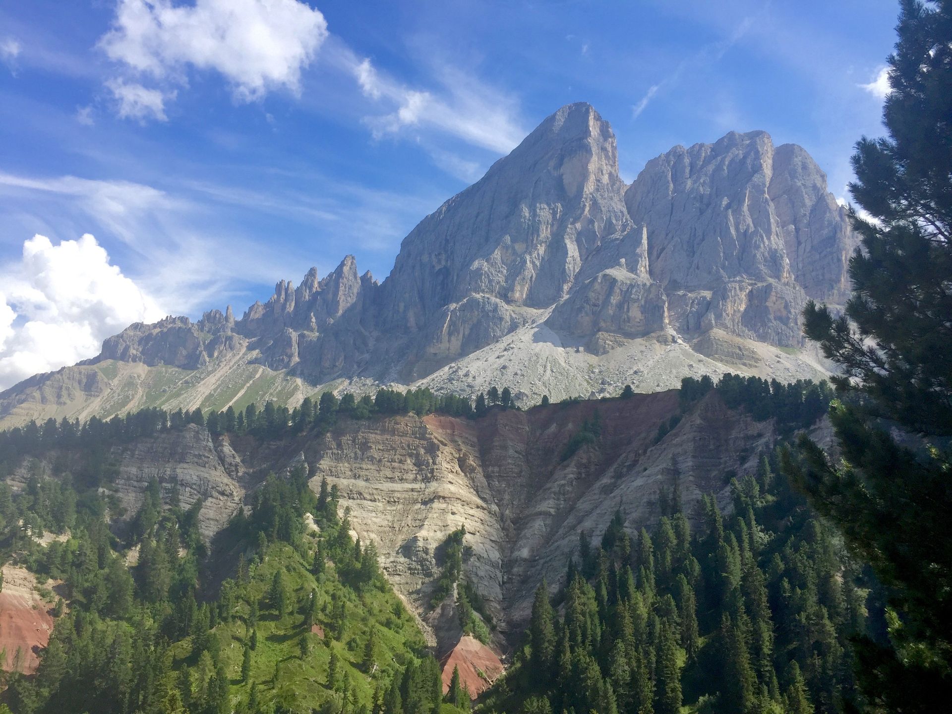 Jagged mountain peaks above a forested valley under a blue sky with scattered clouds