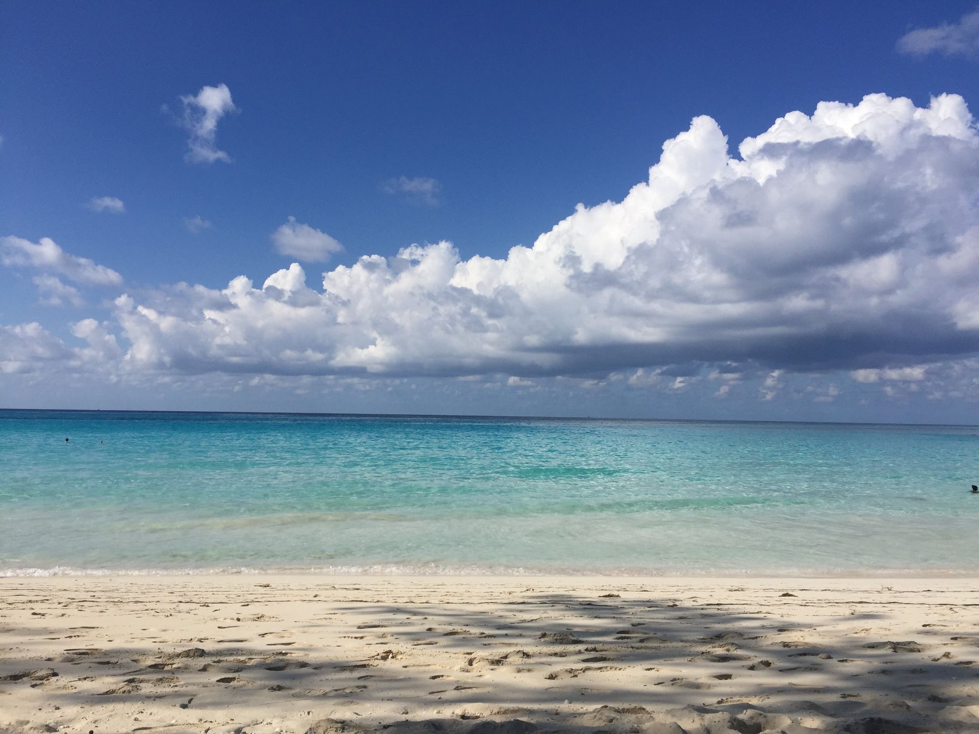 Tropical beach with white sand, turquoise water, and large white clouds in a blue sky
