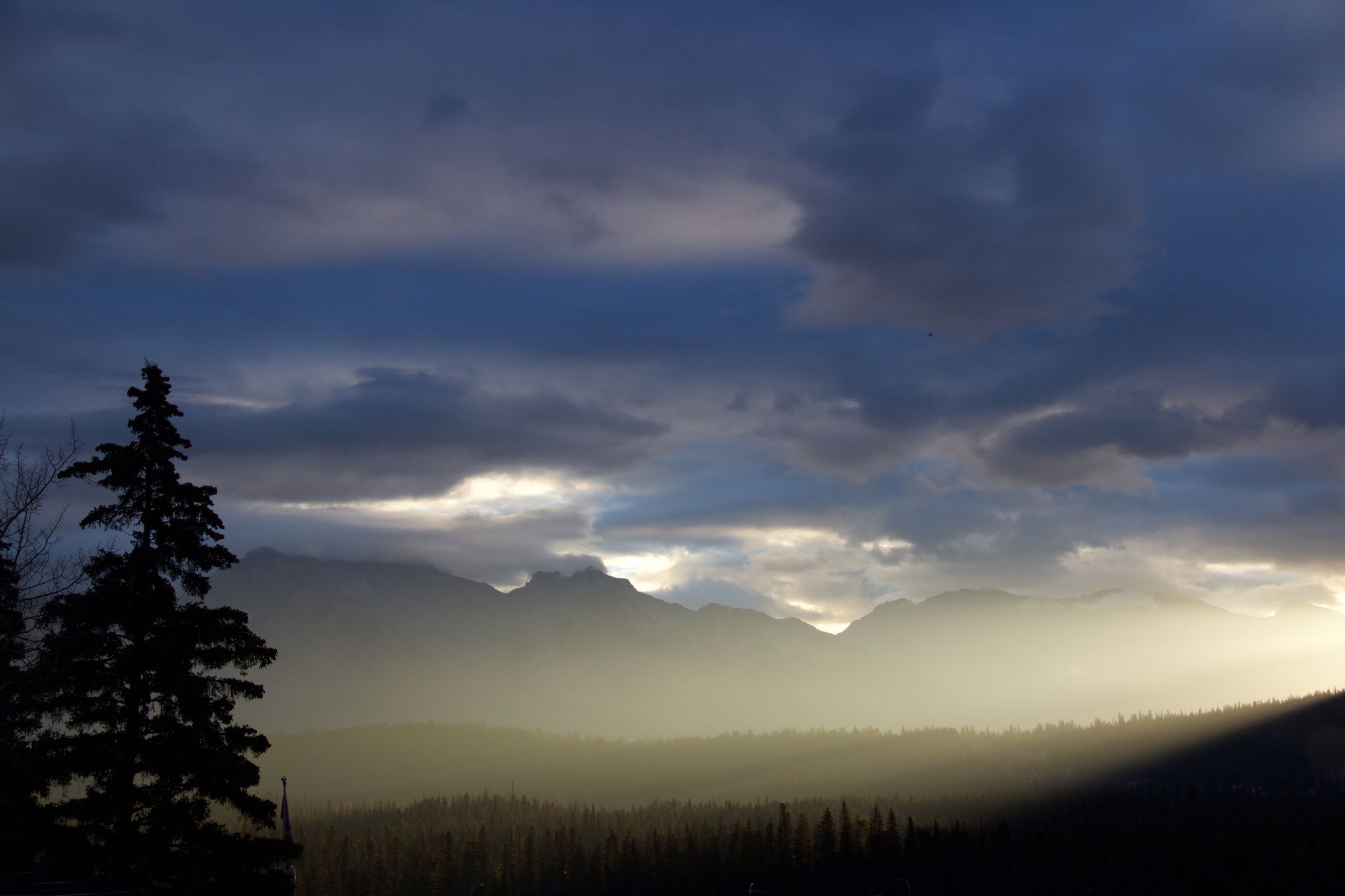 Dramatic cloudy sunrise over misty mountain silhouettes and dark pine trees
