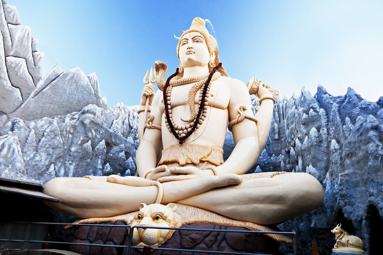 Snow-covered Shiva statue in meditation, with a blue sky and frosty mountains in the background