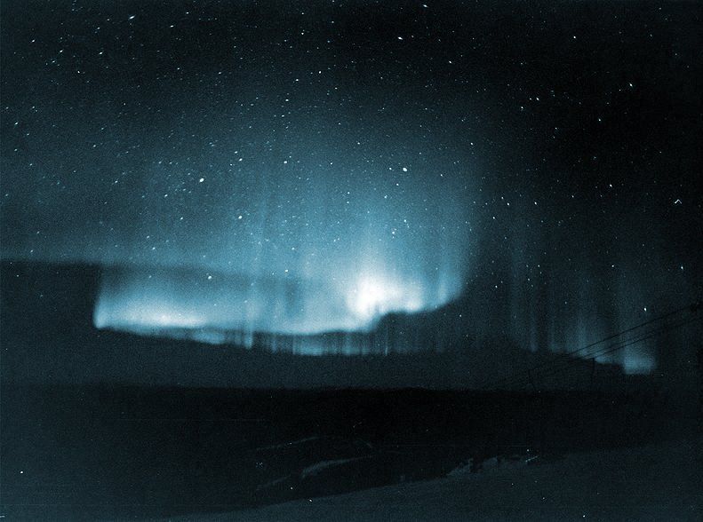 Blue aurora glowing over a dark snowy landscape at night