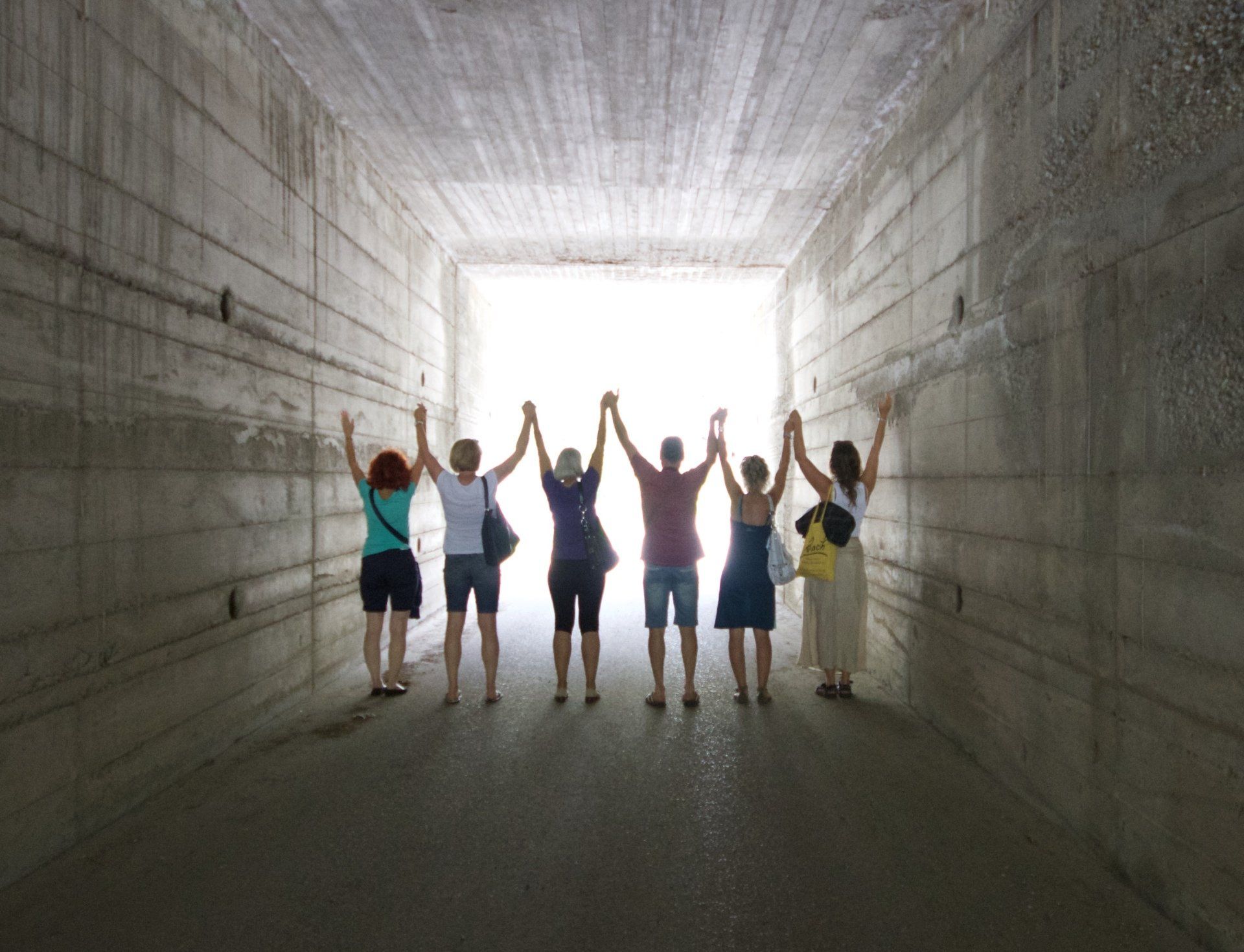 People standing with raised hands in a concrete tunnel, silhouetted by bright light at the exit.