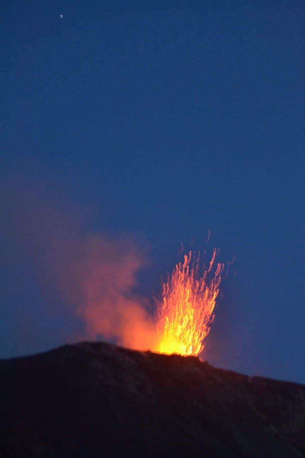 Un vulcano è in eruzione di notte con un cielo azzurro sullo sfondo.
