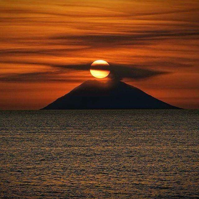 Il sole tramonta dietro un vulcano in mezzo all'oceano.