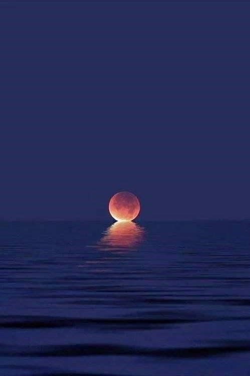 Una luna piena sorge sull'oceano di notte.