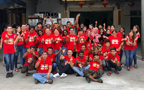 Group of people in red shirts posing outdoors, many giving thumbs-up.