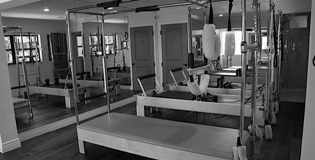A black and white photo of a pilates studio with a lot of mirrors.