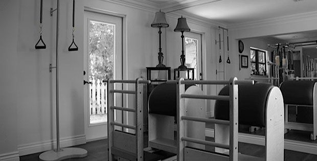 A black and white photo of a pilates studio with exercise equipment.