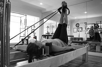 A woman is laying on a pilates machine in a gym.