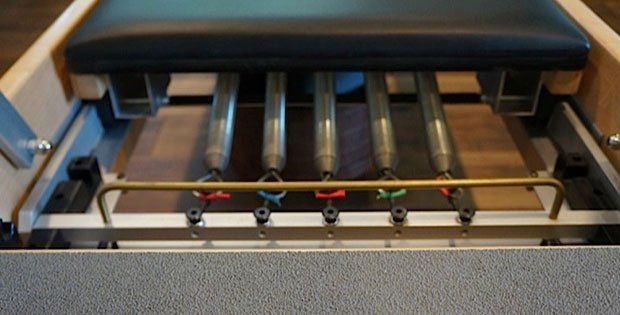A close up of a pilates machine with a bunch of springs on it.